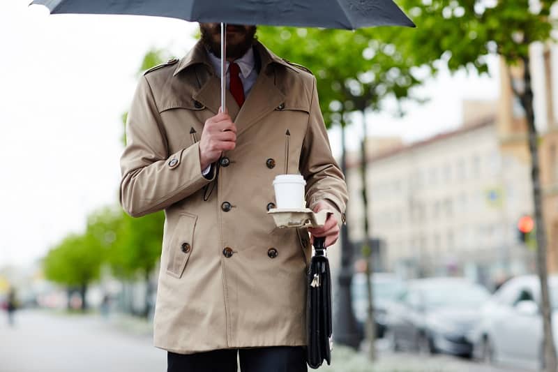 Businessman,sous,parapluie,transportant,boisson,et,porte-documents